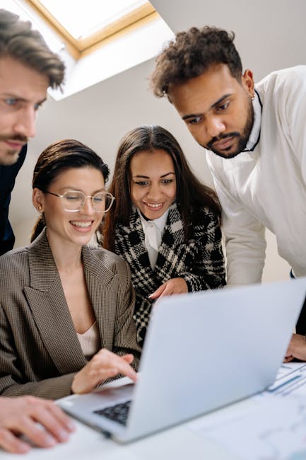 A diverse team of professionals happily collaborating on a laptop at the office.